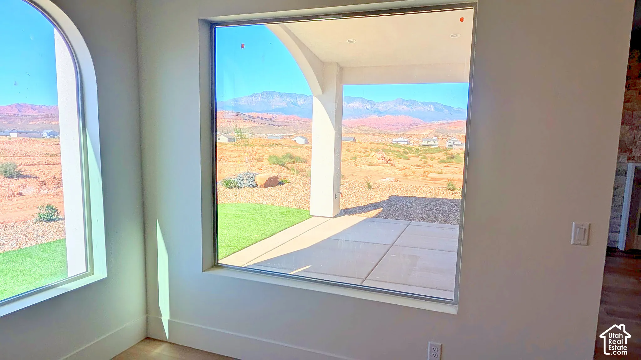 Large picture windows showcasing a covered concrete patio, natural desert landscape, and mountain backdrop