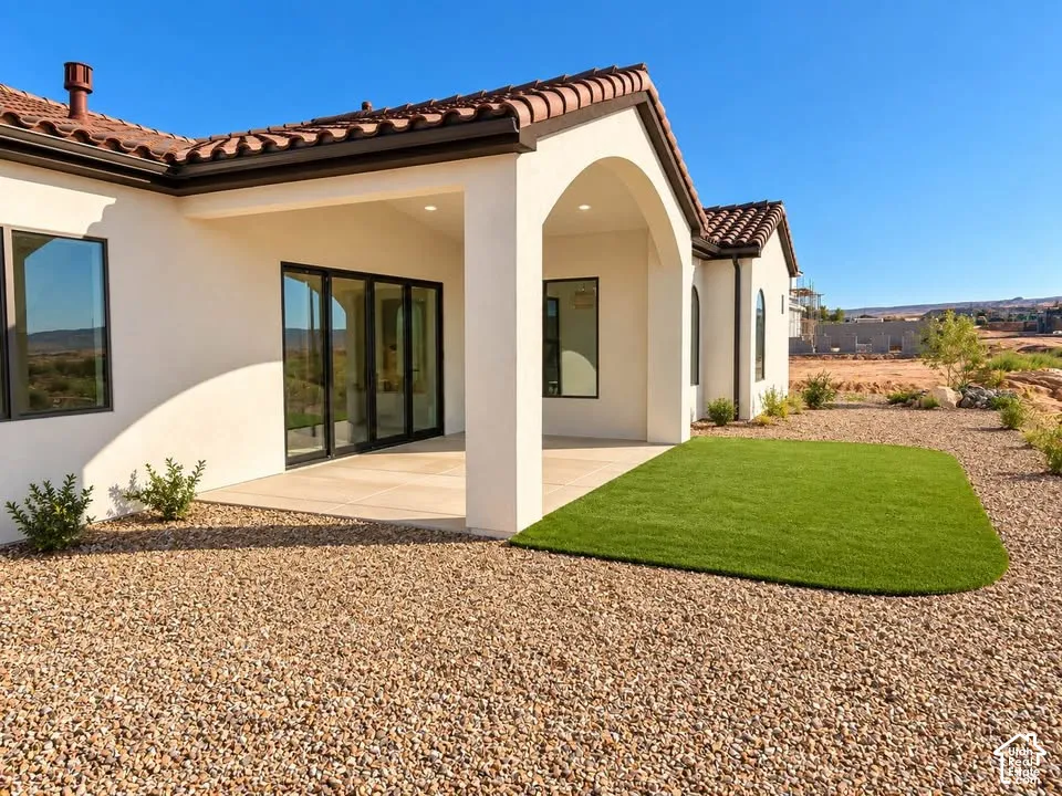 Stucco exterior featuring a covered patio with an arched entryway, tile roof, multi-panel sliding glass doors, and synthetic turf lawn