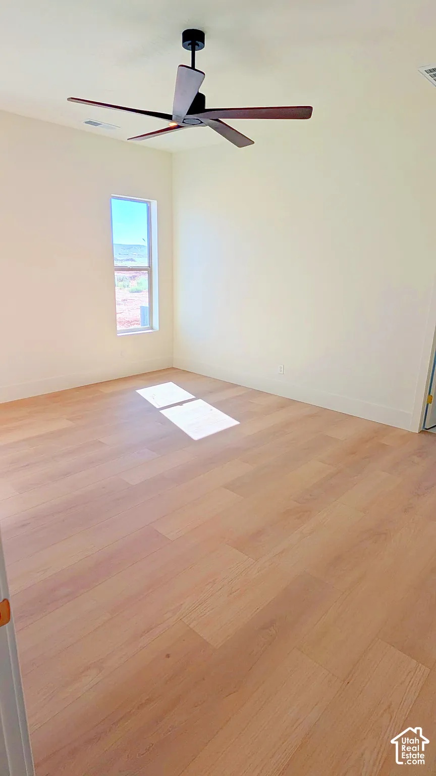 Interior space featuring light-toned wood-finish flooring, neutral wall paint, and a modern ceiling fan with dark blades