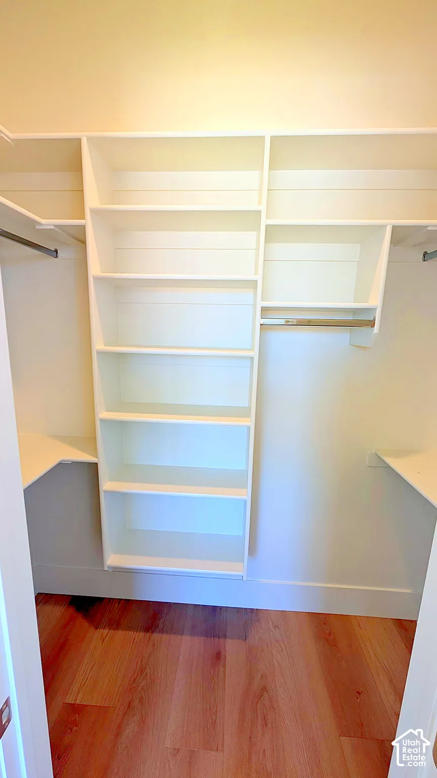 Custom closet organization system featuring white built-in shelving, multiple open-storage compartments, metal hanging rods, and wood-finish flooring