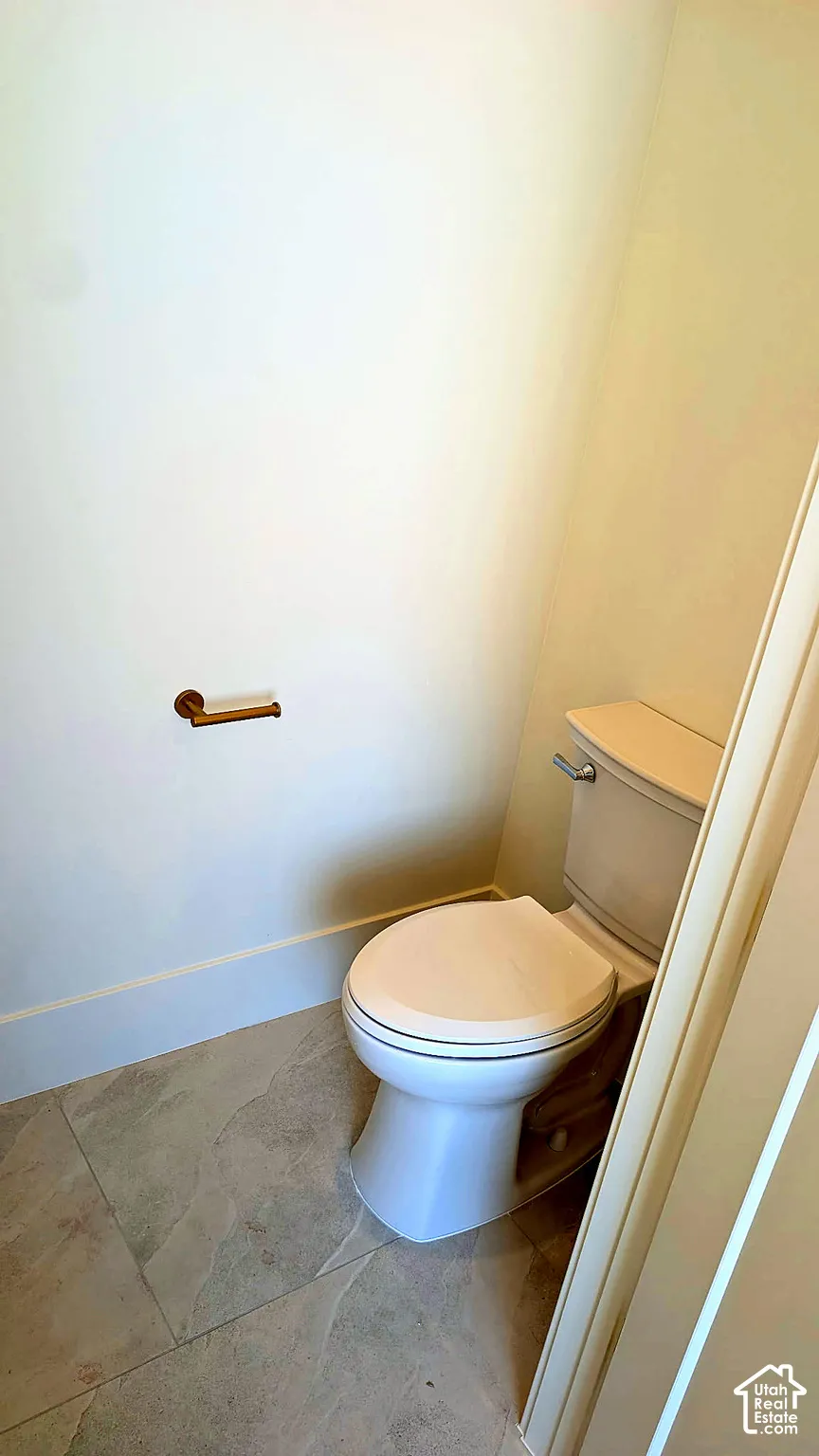 Porcelain toilet with a coordinating seat, wall-mounted metallic paper holder, and neutral-toned stone-finish floor tiling