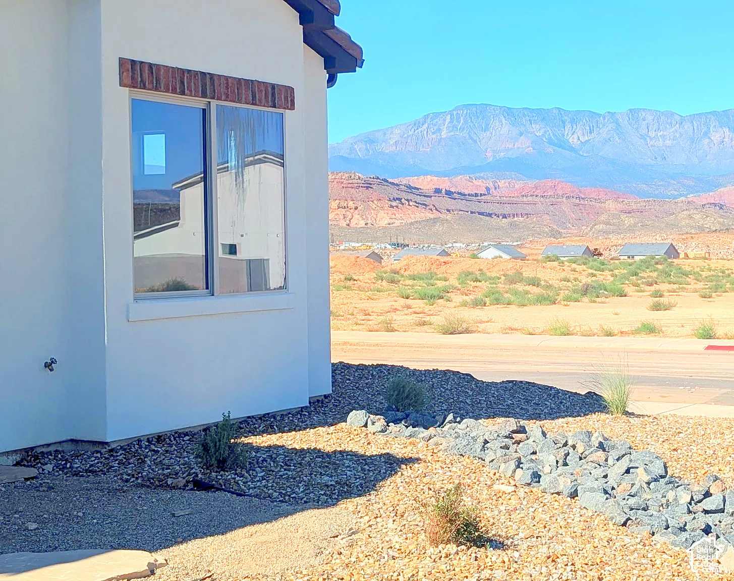 Stucco exterior featuring a masonry window header, double-pane window, and xeric landscaping with decorative rock accents, set against a mountainous backdrop
