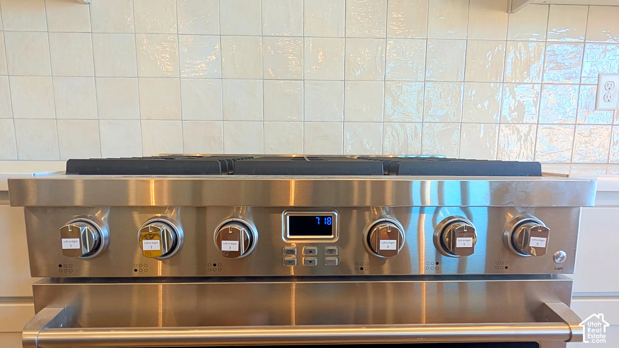 Stainless steel gas range featuring six burners, heavy-duty cast iron grates, digital display, and a tile backsplash