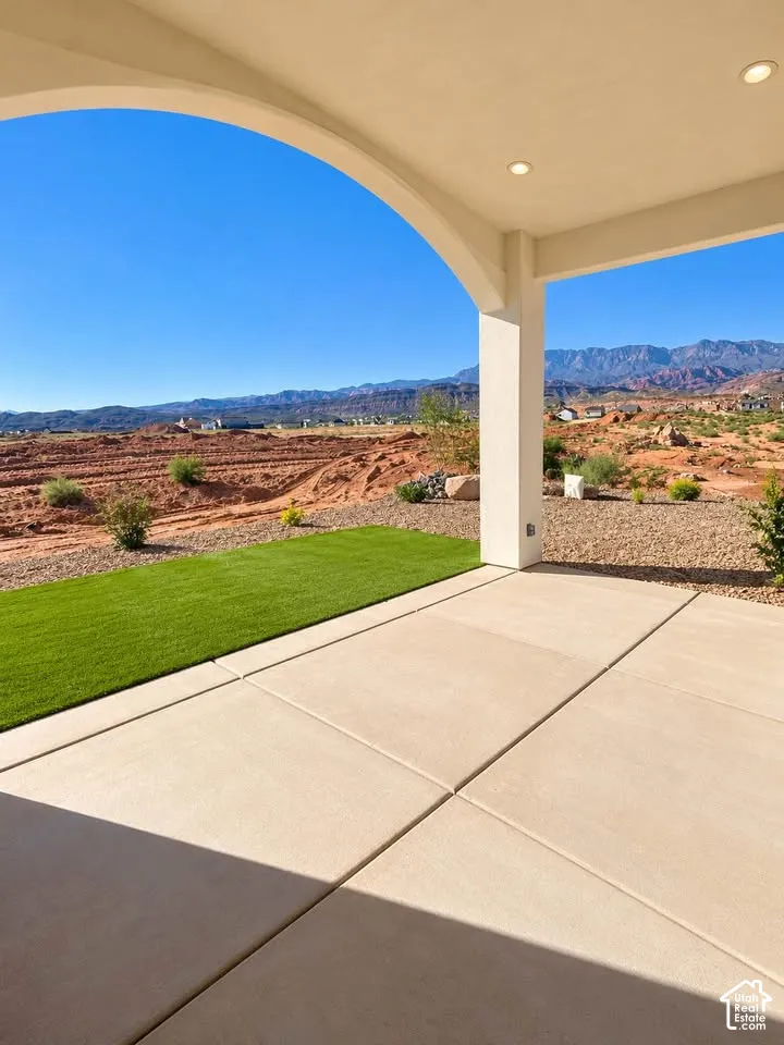 Covered patio with an arched architectural detail, recessed lighting, concrete flooring, artificial turf, and mountain backdrop