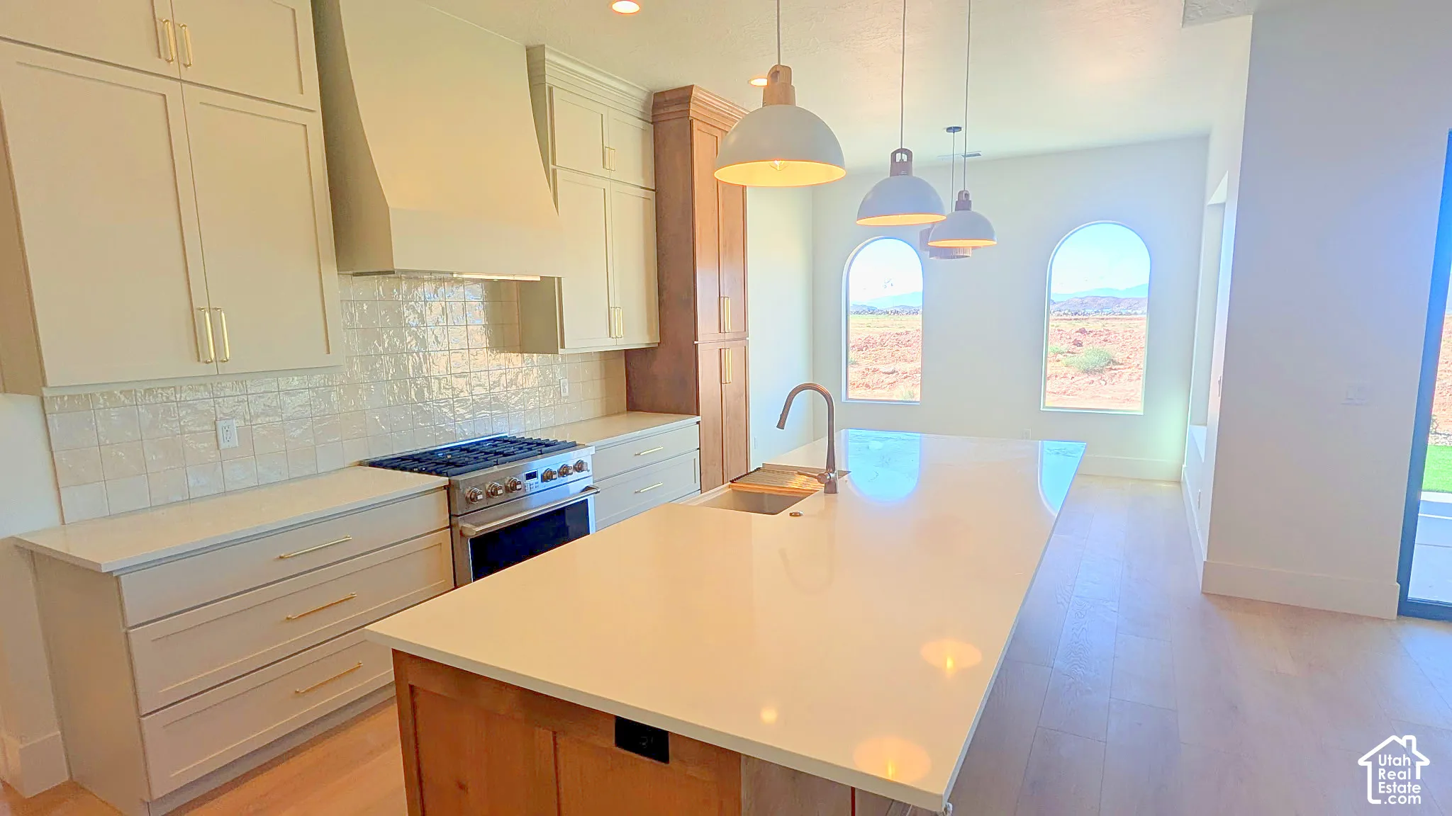 Kitchen featuring a spacious island with a solid-surface countertop, light-toned custom cabinetry, a stainless steel gas range, arched windows, and wood-finish flooring