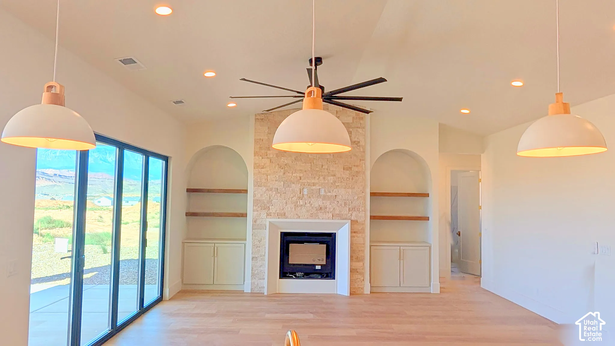 Stone-clad fireplace with custom built-in cabinetry, arched shelving, wood-finish flooring, recessed lighting, and expansive glass sliding doors