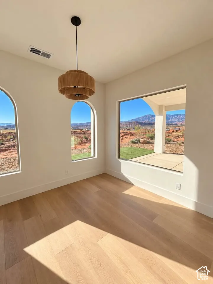 Light-filled room featuring wood-finish flooring, a tiered woven pendant light, two arched windows, and a large picture window showcasing mountain scenery