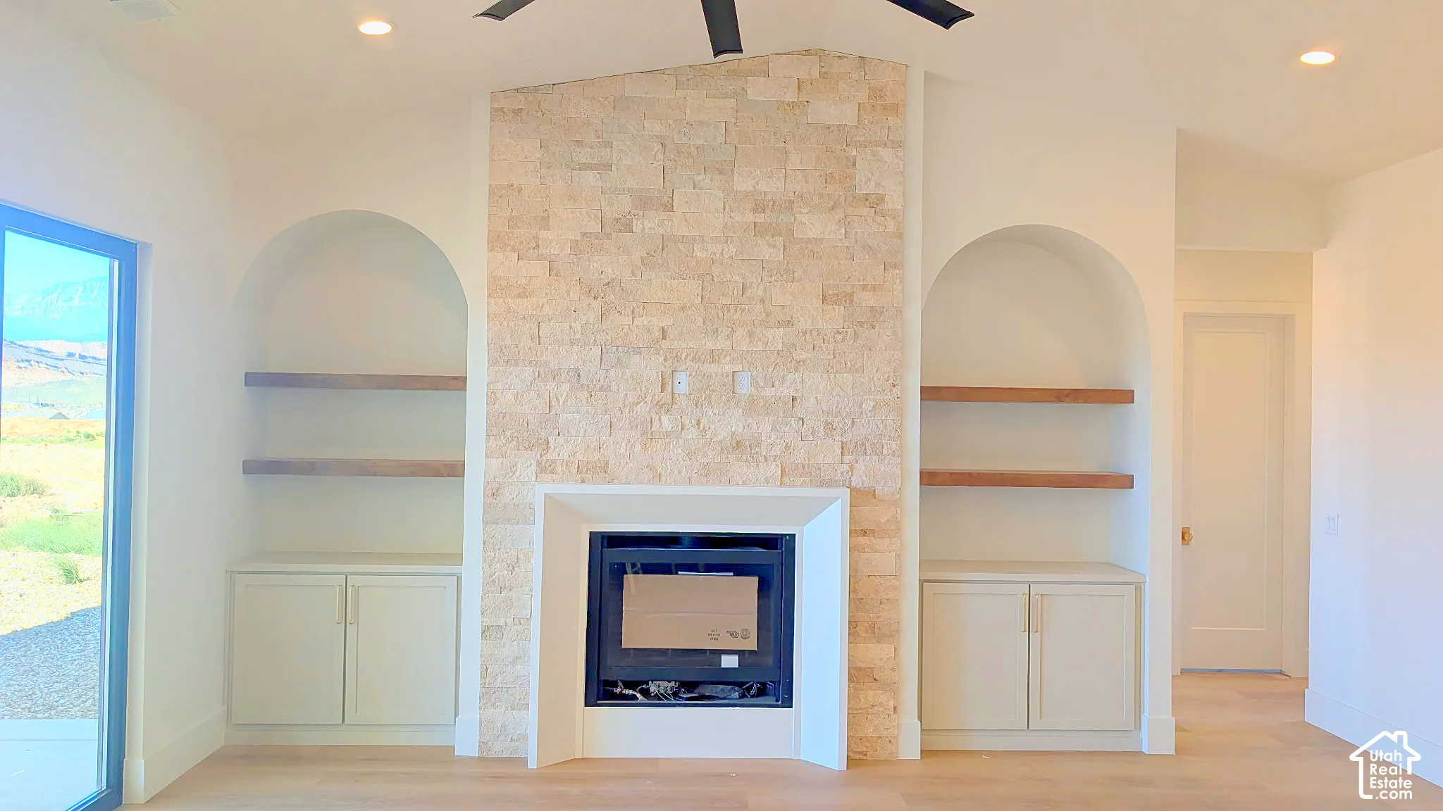 Fireplace surround featuring textured natural stone, arched built-in shelving, lower cabinet storage, and wood-finish flooring