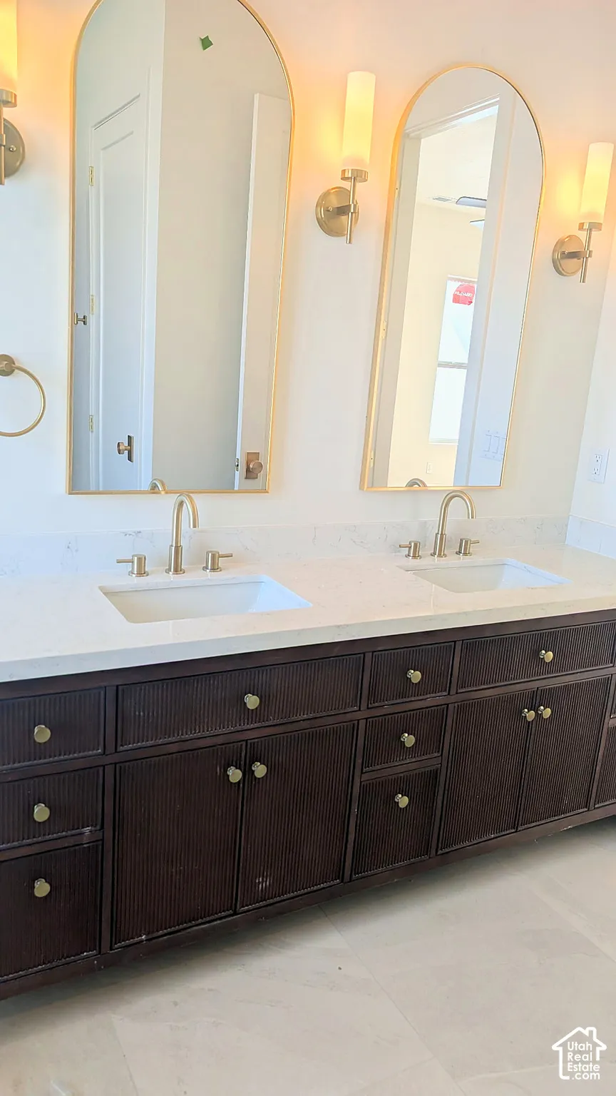 Dual-sink vanity featuring reeded dark-wood cabinetry, light-toned stone countertop, arched gold-rimmed mirrors, and gold-finish wall-mounted light fixtures