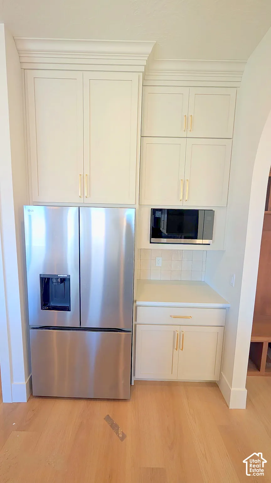Off-white cabinetry with crown molding, gold-finish hardware, built-in stainless steel microwave, integrated refrigerator, and wood-finish flooring