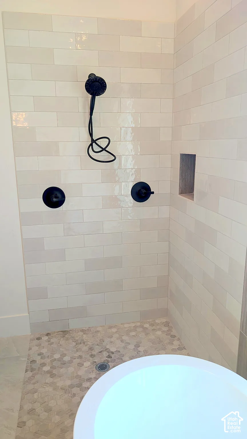 Shower enclosure featuring matte black fixtures, elongated wall tiling in a brick pattern, a recessed storage niche, and a stone-tiled floor