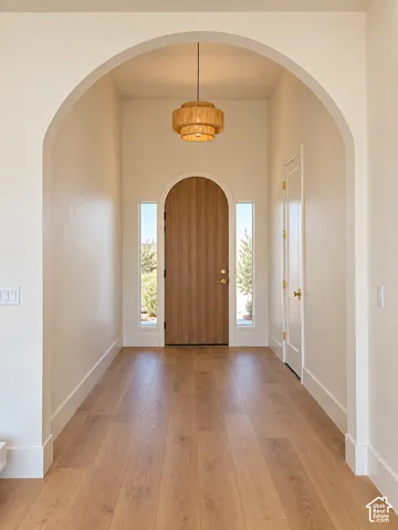 Arched entryway featuring a pendant light fixture, wood-finish flooring, an arched wood door, and flanking vertical windows