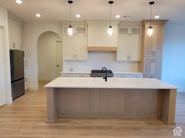 Kitchen with a center island, pendant lighting, stainless steel refrigerator, and wood-finish flooring