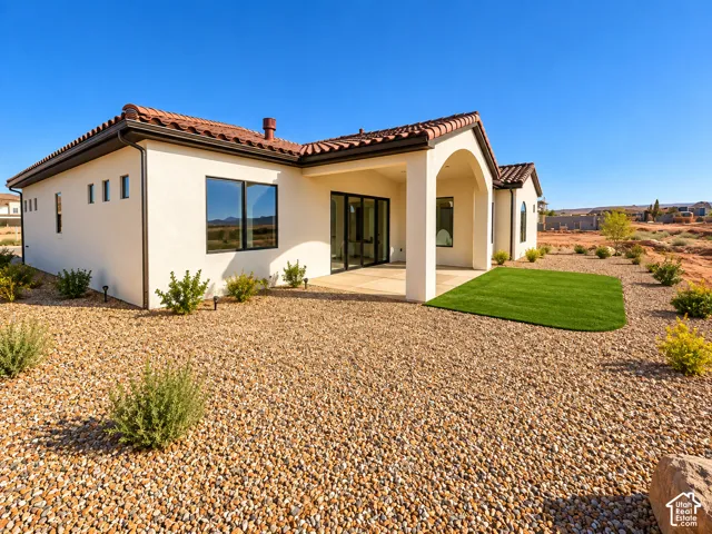 Stucco exterior with a terracotta tile roof, covered patio, gravel landscaping, and a rectangular patch of artificial turf
