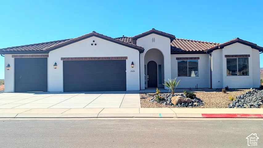 Stucco exterior featuring a concrete tile roof, arched entryway, multi-car garage, and desert-inspired landscaping