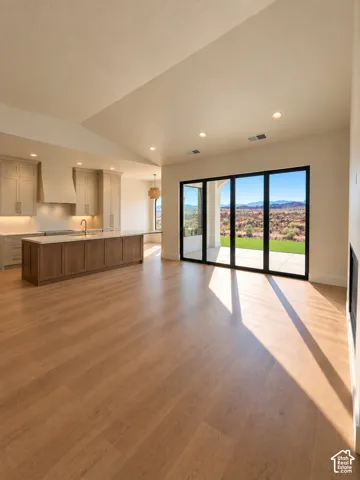 Vaulted ceiling with recessed lighting, wood-finish flooring, kitchen island with wood cabinetry, light-toned kitchen cabinetry, and expansive sliding glass doors