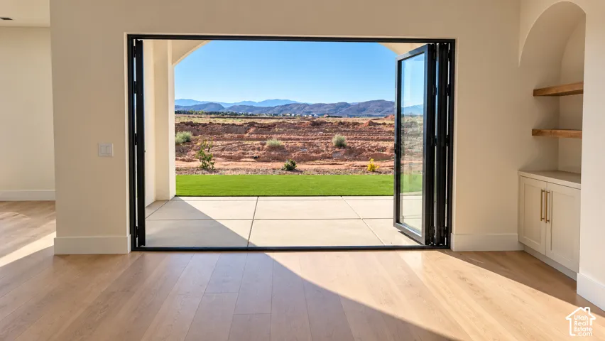 Expansive folding glass doors opening to a concrete patio, wood-finish flooring, and built-in shelving with lower cabinetry