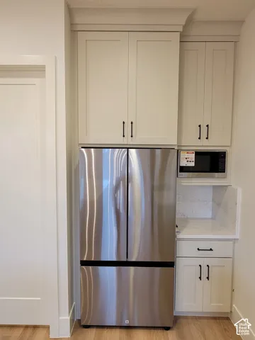 Stainless steel refrigerator, upper and lower cabinetry, built-in microwave, stone countertop, wood-finish flooring
