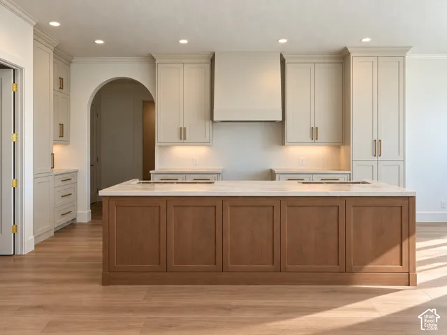 Kitchen featuring a large central island with a light-colored countertop, recessed lighting, wood-finish flooring, two-tone cabinetry with brass hardware, and an arched entryway