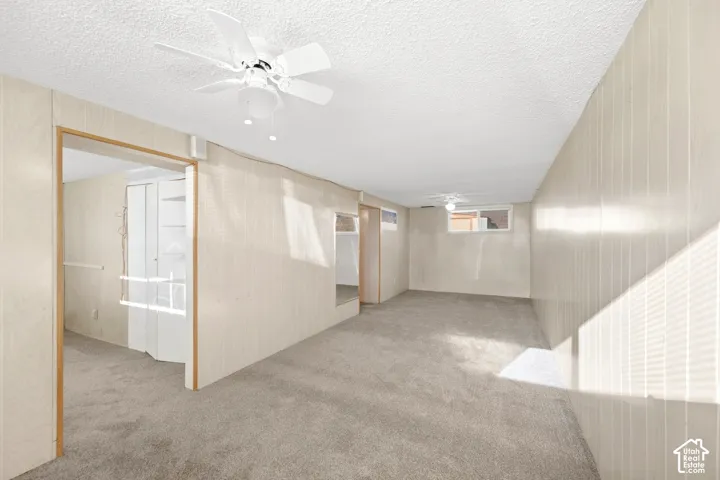 New carpeted flooring throughout, textured ceiling, two ceiling fans with light fixtures, and paneled wall finish