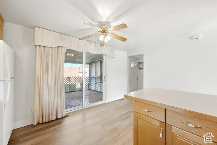 Wood-finish flooring throughout, ceiling fan with light fixture, sliding glass door leading to an enclosed porch, and a built-in island with cabinet storage