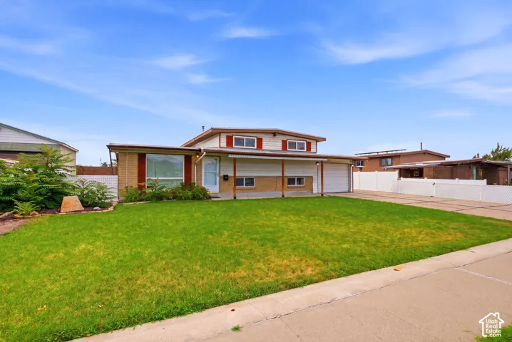 Expansive front lawn, attached carport, two-car garage, brick facade detailing, and white vinyl fencing