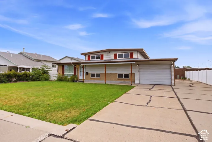 Expansive concrete driveway, attached garage, well-maintained front lawn, white vinyl fencing, and brick facade accents
