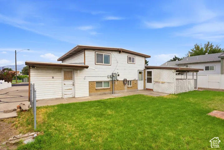 Expansive green lawn, white horizontal siding, lower-level windows, covered patio structure