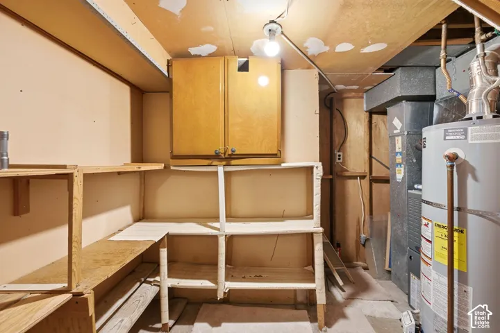 Utility room featuring built-in wooden shelving, a wall-mounted wooden cabinet, and exposed mechanical systems