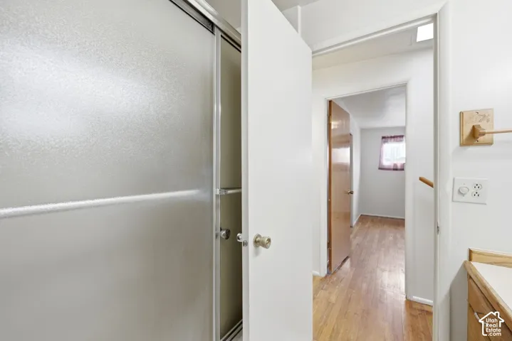 Sliding frosted shower door, wood-finish flooring, and natural wood cabinetry