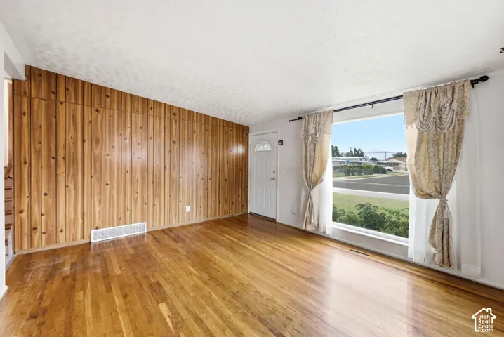 Wood-finish flooring with a wood paneled accent wall, a white entry door, and a large front-facing window