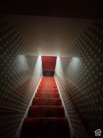 Staircase with patterned wall covering, red carpeted steps, and a wooden handrail