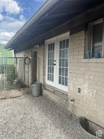 Brick exterior with white double French doors, gravel hardscaping, and a covered patio area
