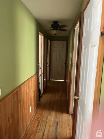 Hallway featuring wood-finish flooring, wood paneling, paneled doors, and a ceiling fan with integrated lighting