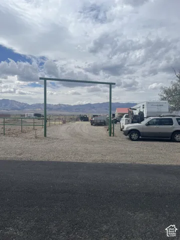 Gravel driveway with a metal archway entry, bordered by a wire fence and distant mountain scenery