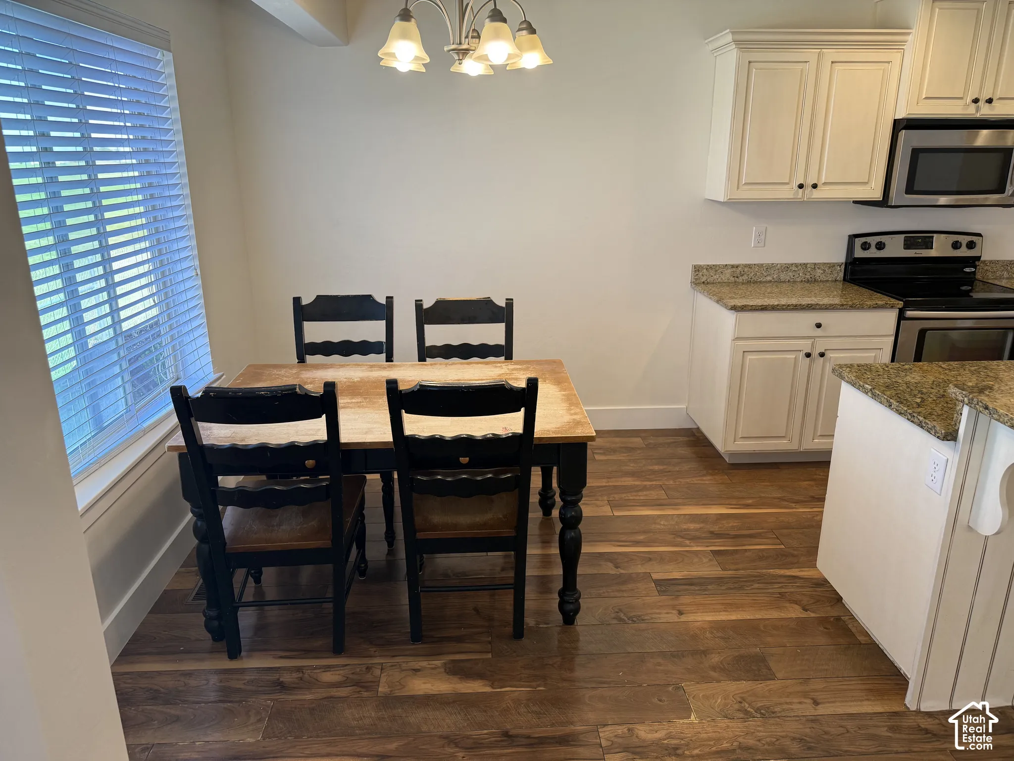 Wood-finish flooring throughout, complemented by white cabinetry with dark pulls, light-toned granite countertops, and stainless steel appliances
