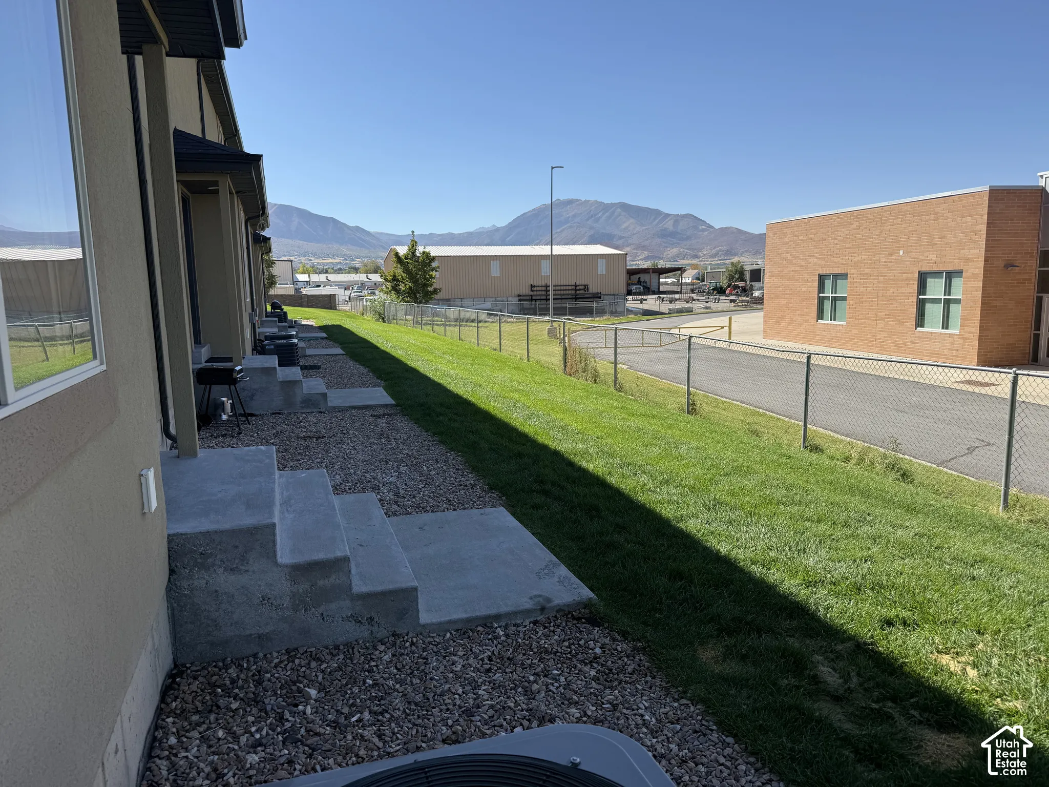Expansive lawn area with a chain-link fence, concrete steps, and gravel landscaping
