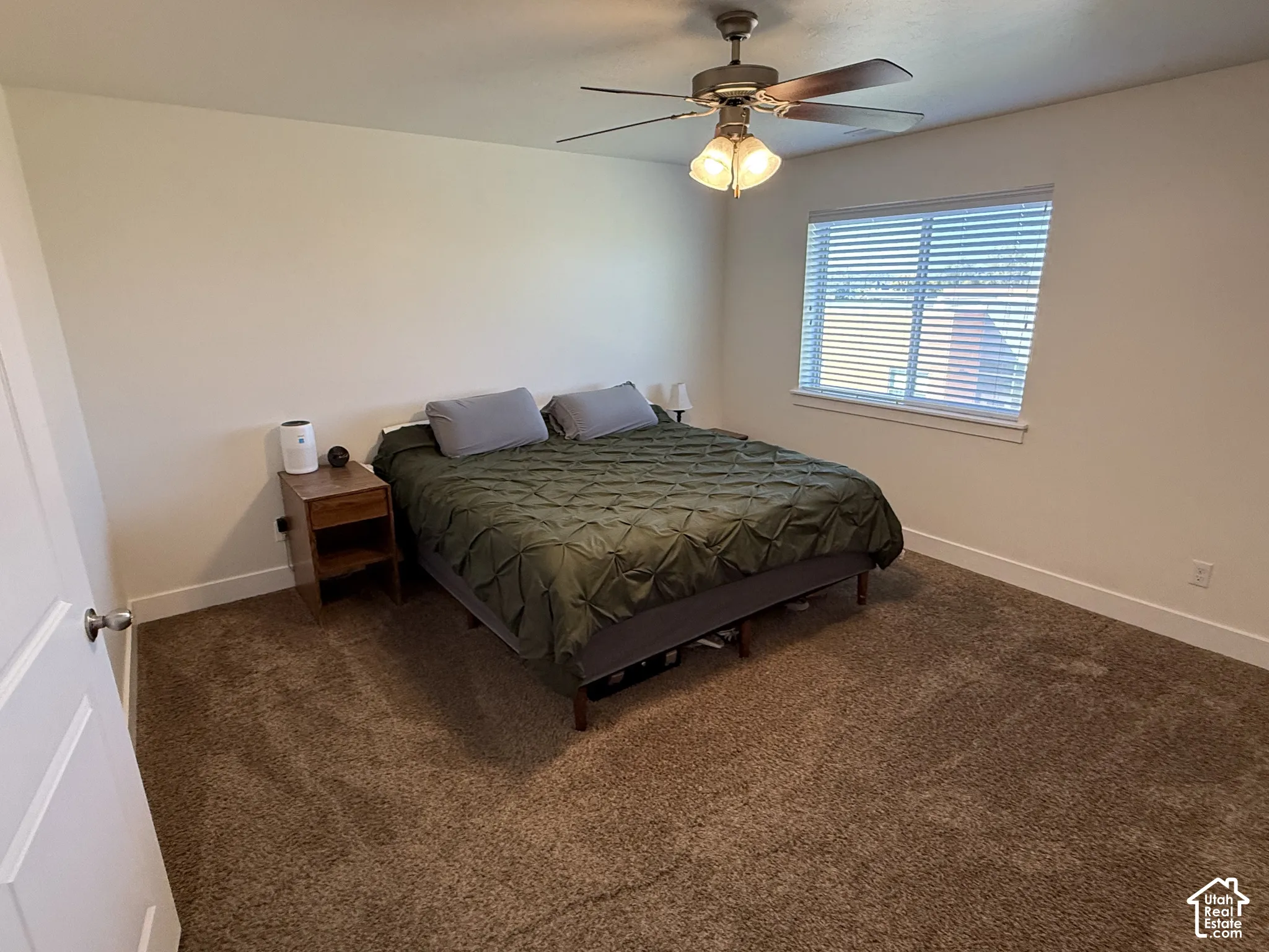 Neutral-toned walls, plush carpeting, ceiling fan with integrated lighting, and a window with blinds