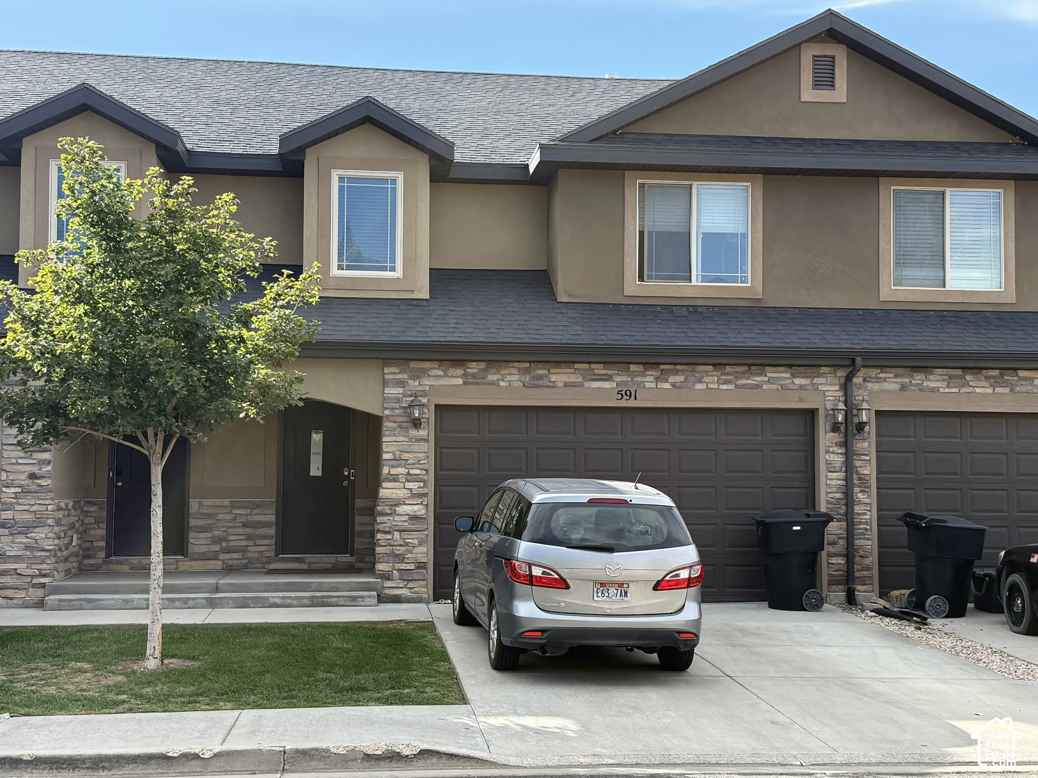 Stone veneer accents, two-car garage, dormer windows, asphalt shingle roof, and a concrete driveway