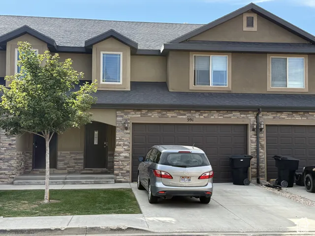 Stone veneer accents, two-car garage, dormer windows, asphalt shingle roof, and a concrete driveway