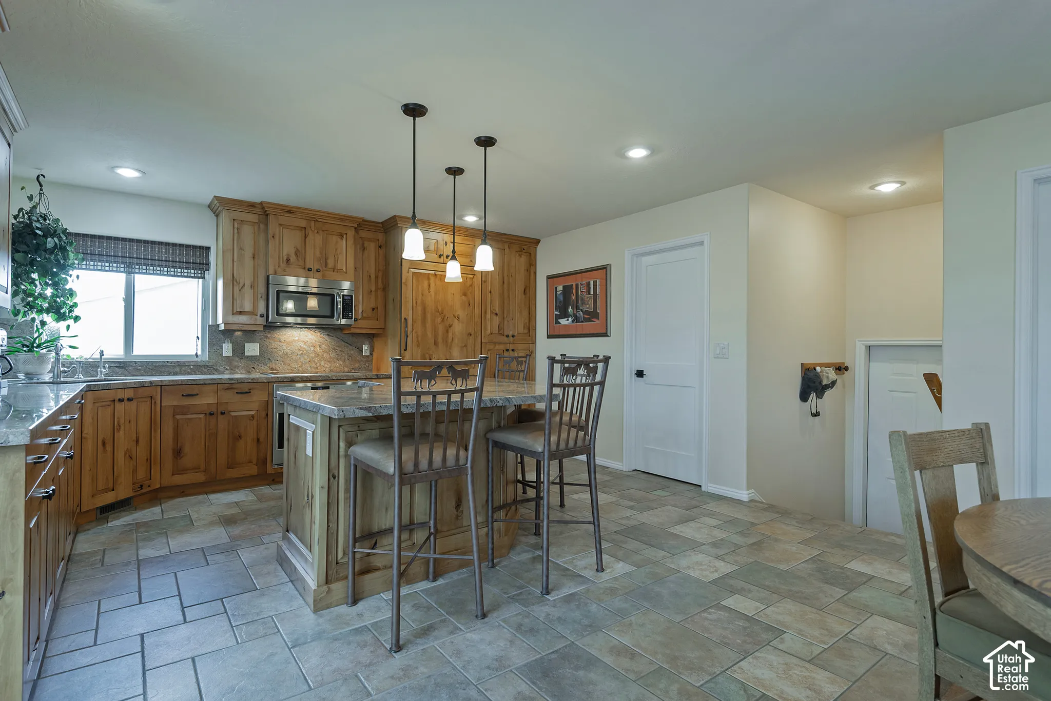 Kitchen featuring wood cabinetry, stone countertops, a stainless steel microwave, an island with pendant lighting, and tiled flooring