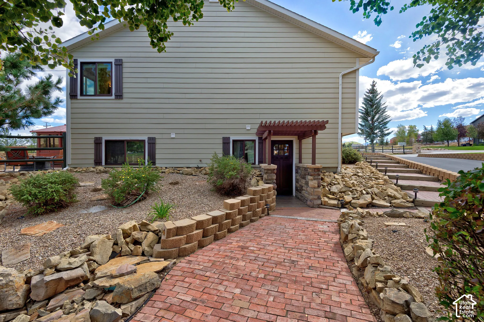 Siding exterior with decorative shutters, brick paver walkway, stone retaining walls, and a pergola entrance