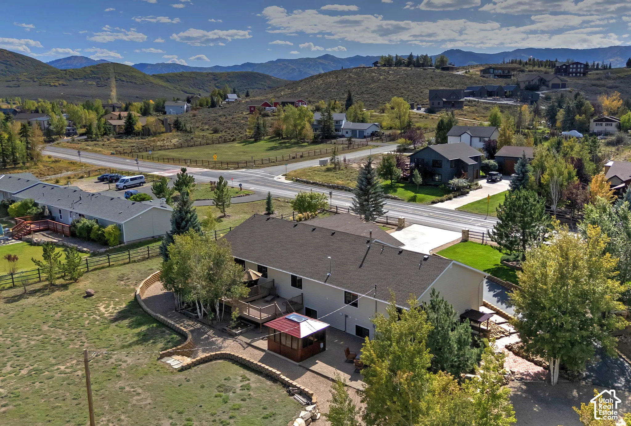Expansive lot with mountain backdrop, featuring a multi-level deck, a built-in fire pit, and a covered patio area