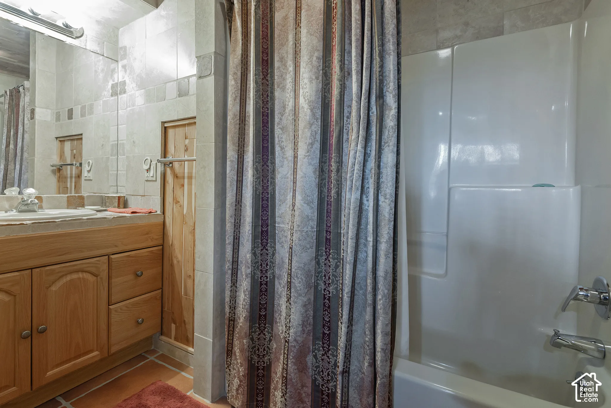 Wood-finish vanity with an integrated sink, large wall-mounted mirror, and tile flooring