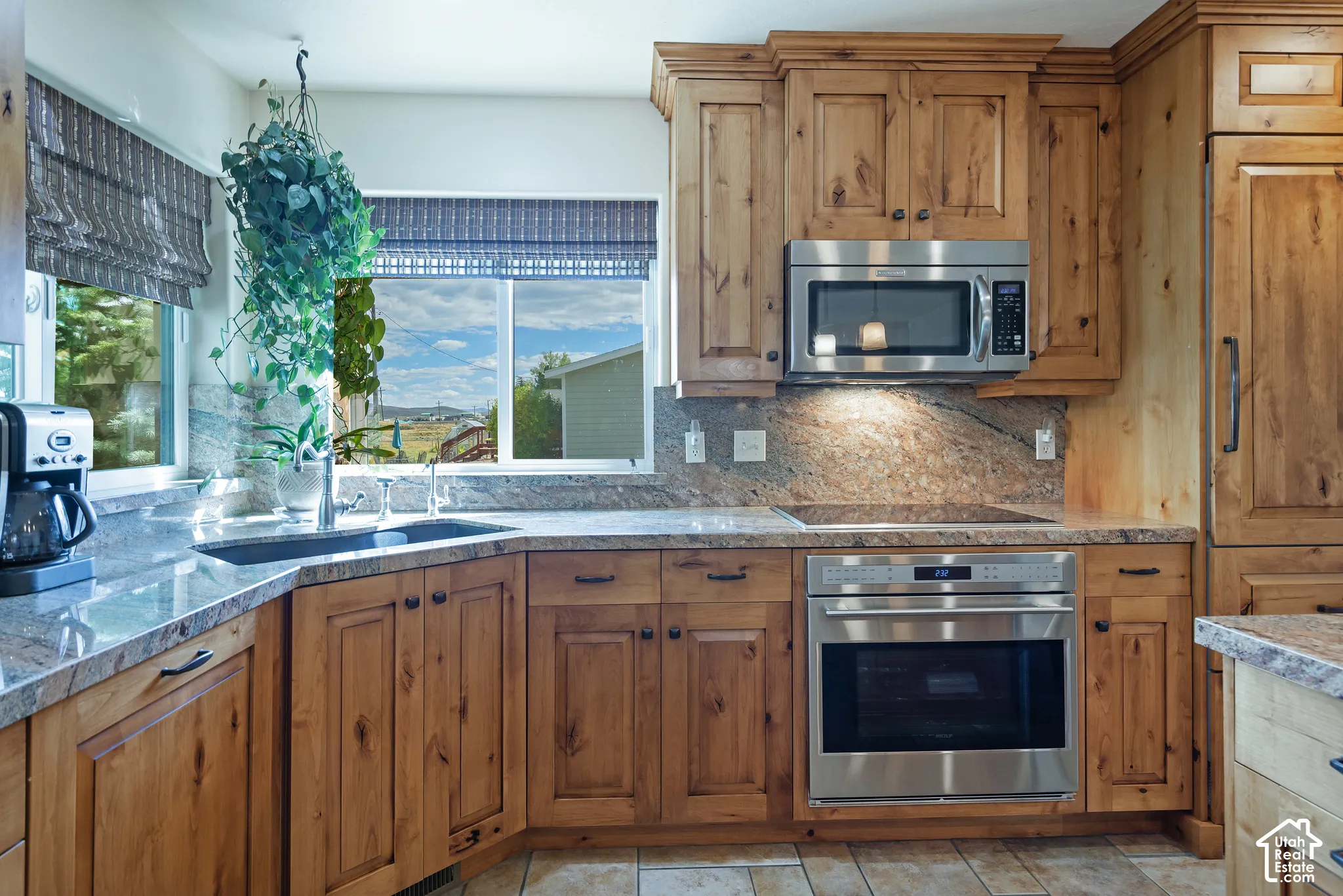 Kitchen featuring natural wood cabinetry, stone countertops, stainless steel appliances, and an undermount sink