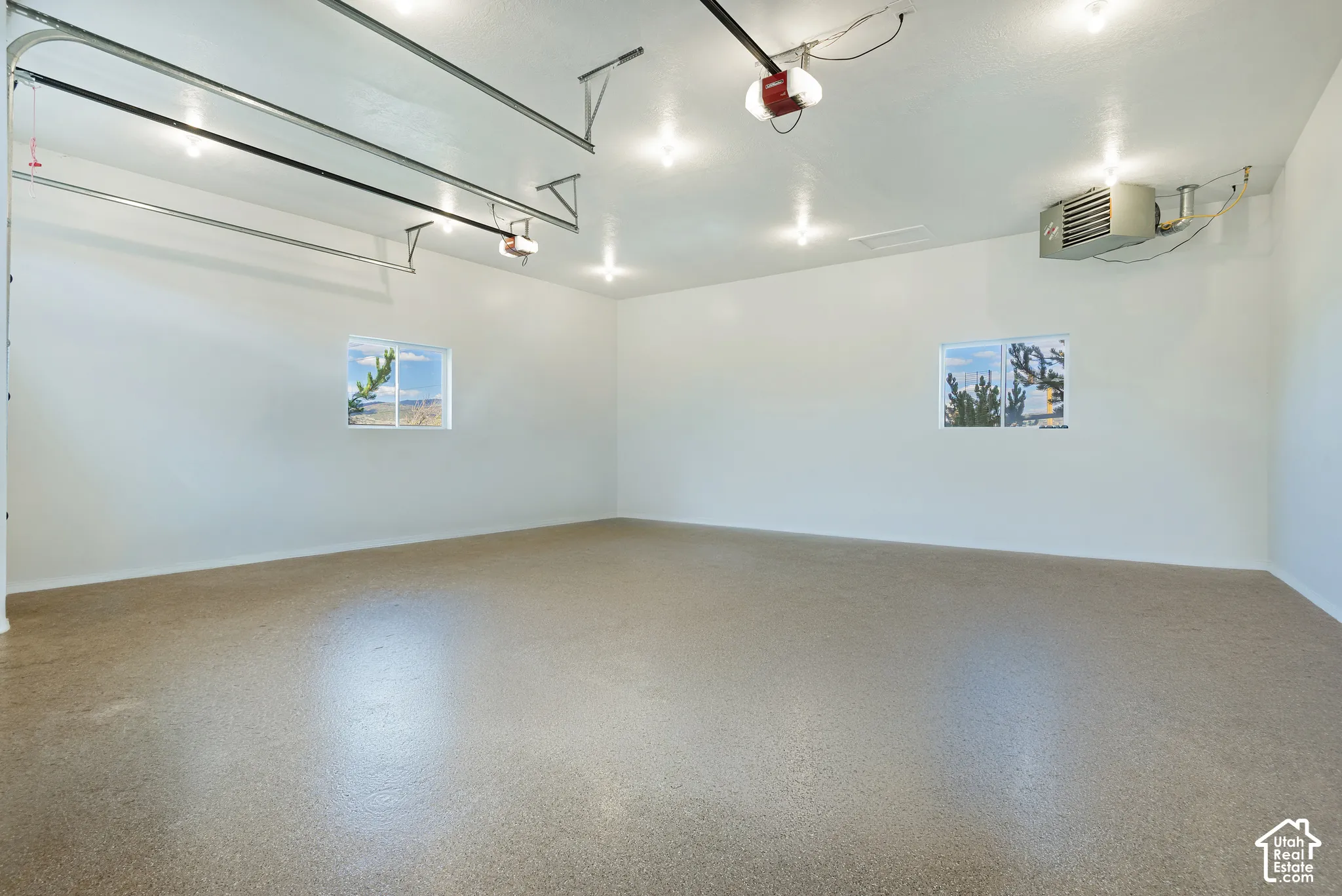 Spacious garage with an epoxy floor, multiple overhead lights, two windows, and an overhead heating unit