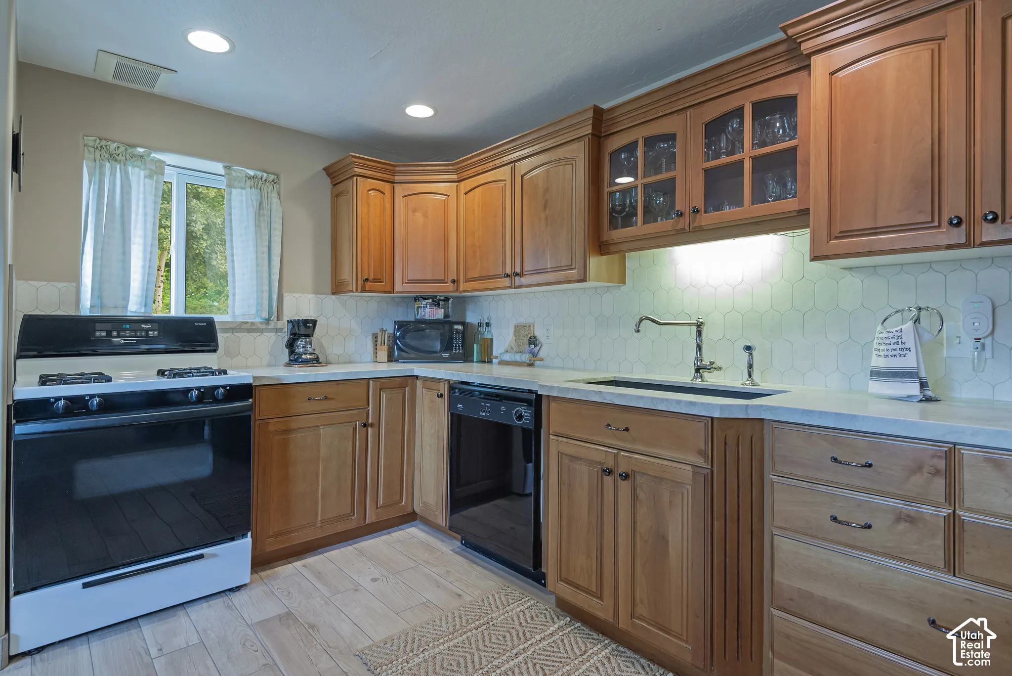 Wood-finish flooring, light-toned countertops, and a geometric tile backsplash