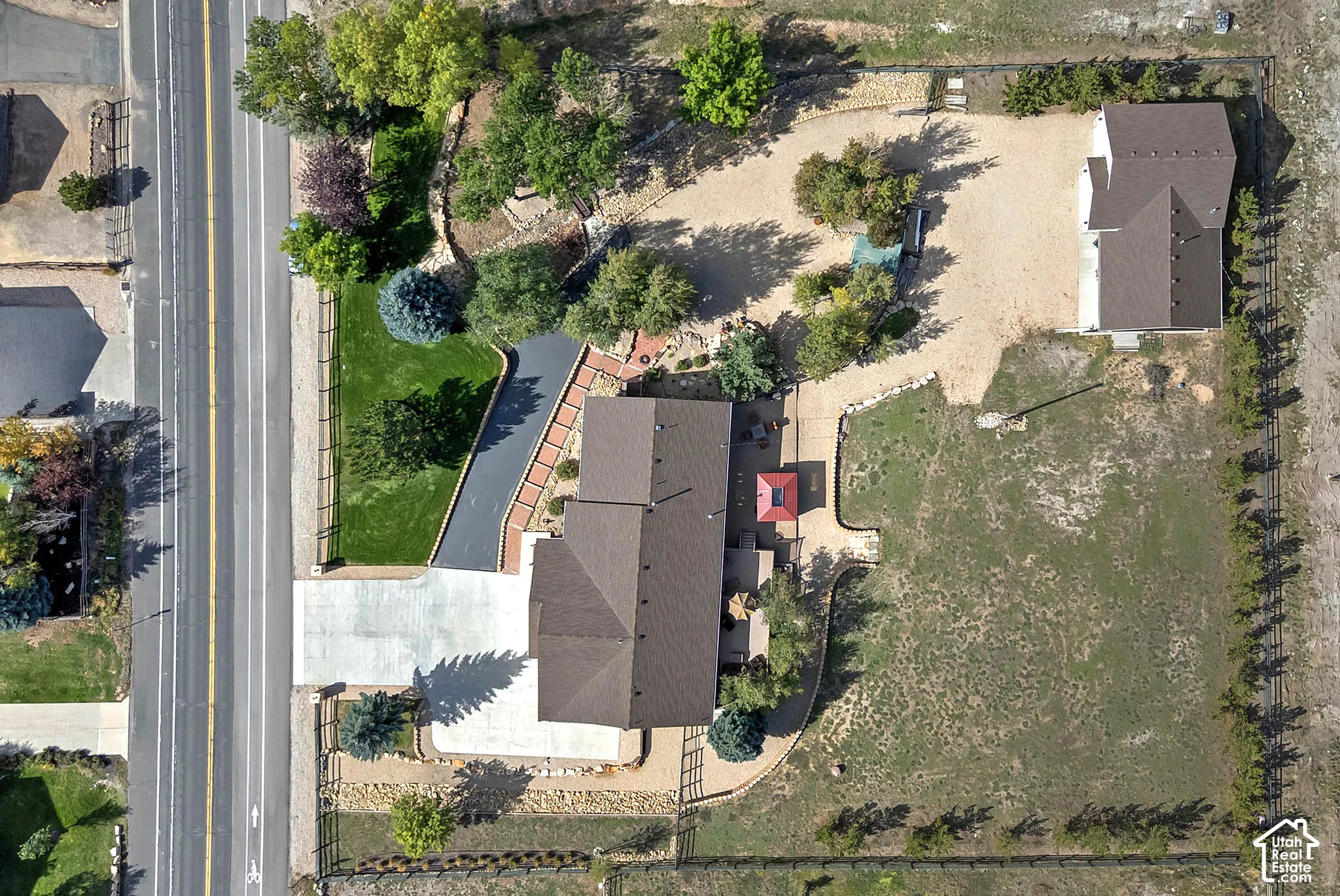 Expansive lot featuring a main residence, secondary detached structure, paved driveway, landscaped front yard with mature trees, and a large unmanicured rear yard