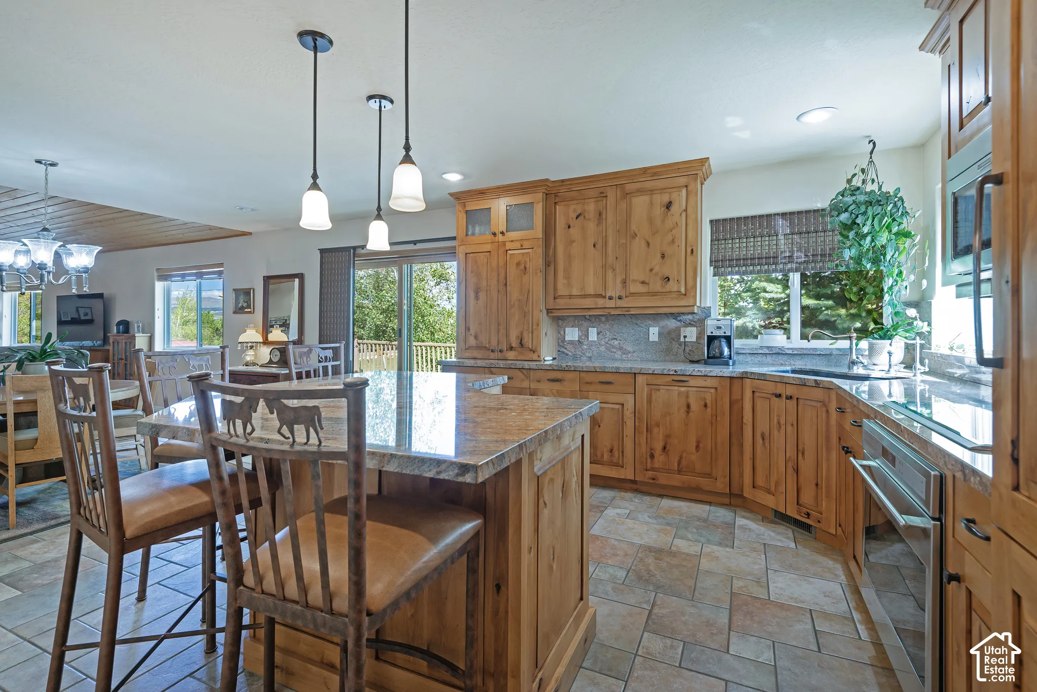 Kitchen featuring wood cabinetry, stone countertops, stainless steel appliances, and a central island with pendant lighting