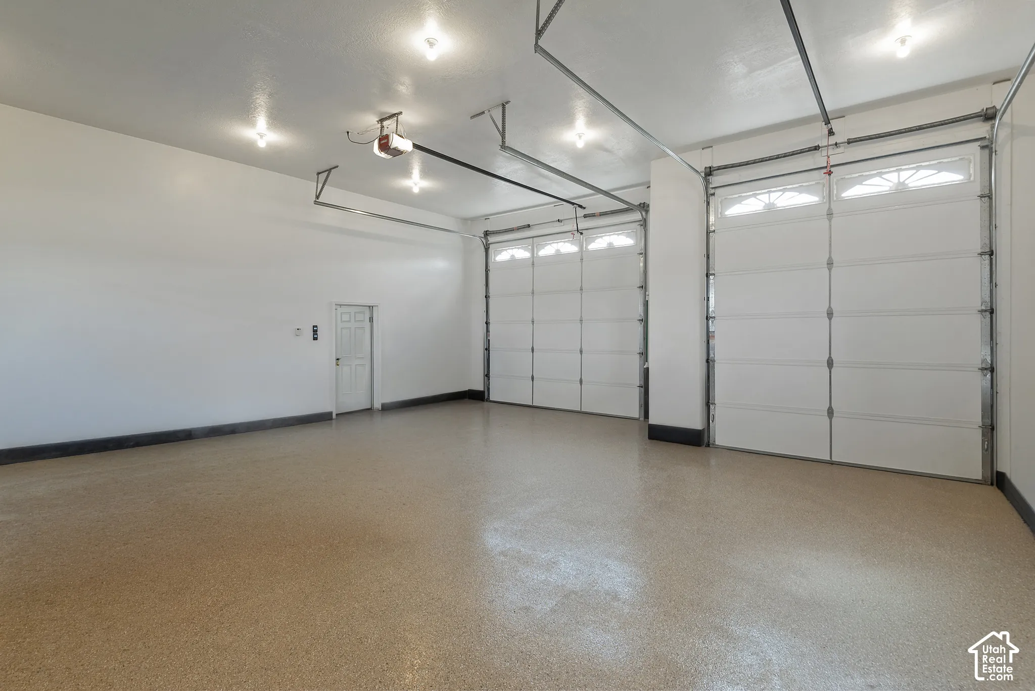Spacious garage featuring two overhead doors, a pedestrian door, multiple ceiling-mounted light fixtures, and a durable epoxy-coated concrete floor